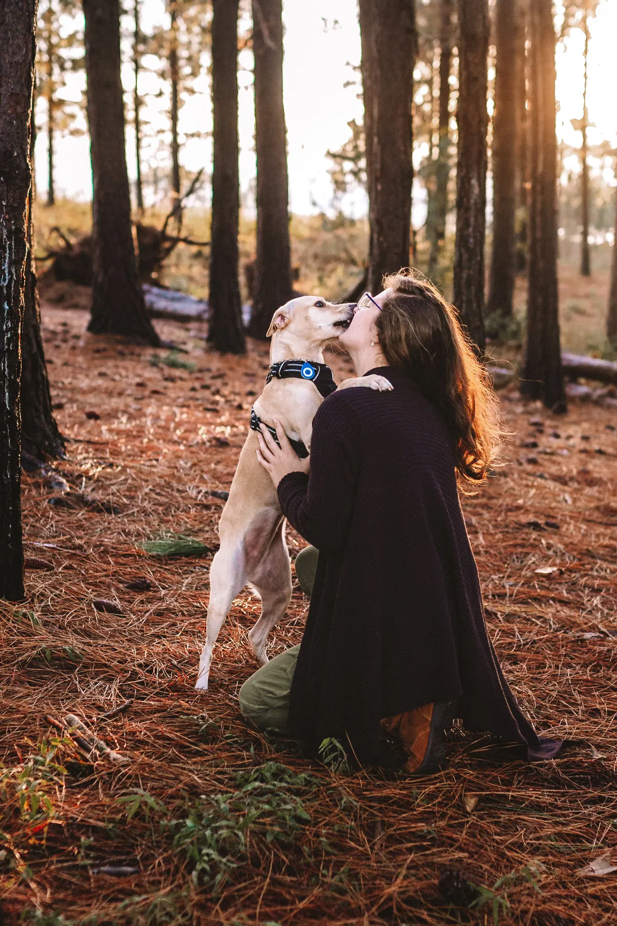 Vitória ajoelhada no bosque, com uma cachorra pulando em seus braços
