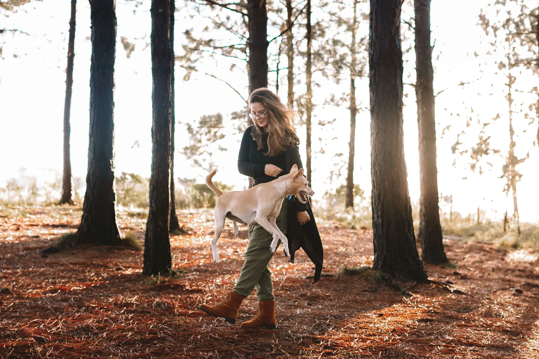 Vitória caminhando no bosque com uma cachorra pulando ao seu lado